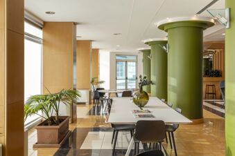 Bright seating area with white tables, black chairs, green columns, and potted plants inside B&B Hotel Cuneo Cristal