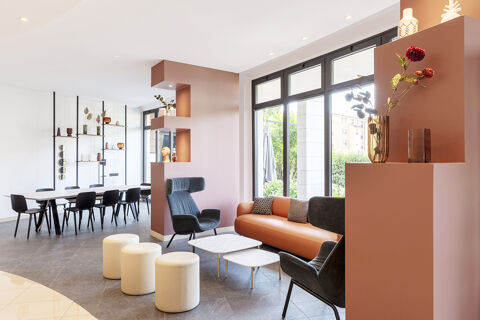 Modern lobby area of B&B Hotel Sassuolo with black armchairs, a brown sofa, white stools, and large windows showing outdoor greenery