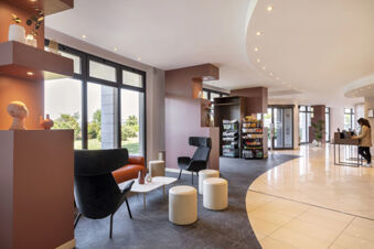 Modern hotel lobby at B&B Hotel Sassuolo with seating area, snack shelves, large windows, and a person using a computer
