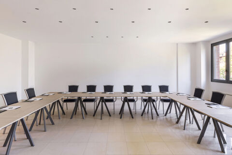 Meeting room at B&B Hotel Sassuolo with U-shaped tables, black chairs, white walls, tiled floor, and a large window on the right