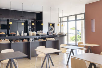 Dining area with light wood tables and chairs and a buffet counter with pastries and cereals at B&B Hotel Sassuolo