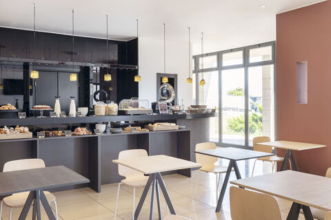 Dining area with light wood tables and chairs and a buffet counter with pastries and cereals at B&B Hotel Sassuolo