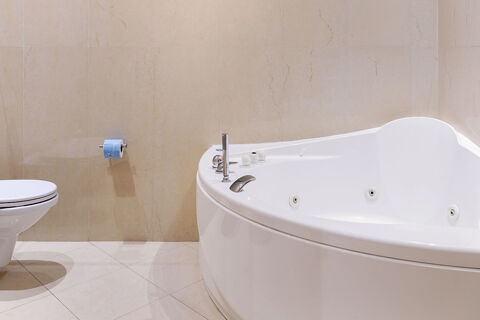 White corner jacuzzi bathtub and a toilet with a blue toilet paper roll on beige tiled walls and floor in B&B Hotel Sassuolo