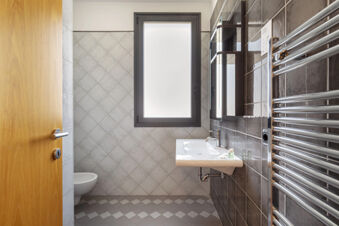 Bathroom interior at B&B Hotel Sassuolo with a wooden door, frosted window, wall-mounted sink, toilet, and heated towel rail