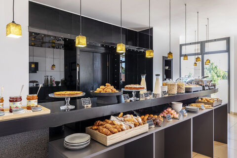 Breakfast buffet with pastries, jam jars, milk bottles, cereals, and utensils on a black counter at B&B Hotel Sassuolo