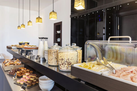 Breakfast buffet with cereals, cold cuts, mini donuts, pastries, and milk bottles at B&B Hotel Sassuolo breakfast area