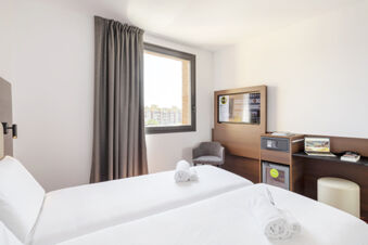 Hotel room at B&B Hotel Sassuolo featuring two beds with white linens, gray curtains, a wall-mounted TV, and a small desk with a laptop