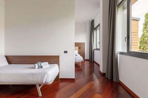 Minimalist hotel room at B&B Hotel Sassuolo with two beds, white linens, wooden floors, large windows, and gray curtains