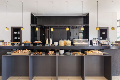 Breakfast buffet with pastries, cereals, milk, plates, and labeled dishes under hanging lights at B&B Hotel Sassuolo