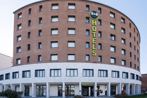 Large curved multi-story brick building with many windows and green B&B Hotel Sassuolo sign on white lower facade and entrance
