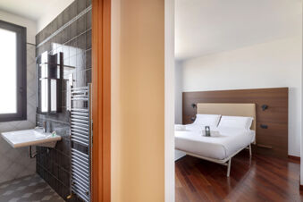 Bathroom with black tiles and sink next to a bedroom with white bed linens and wooden headboard at B&B Hotel Sassuolo
