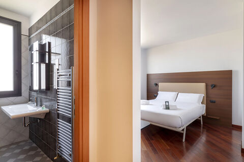 Bathroom with black tiles and sink next to a bedroom with white bed linens and wooden headboard at B&B Hotel Sassuolo