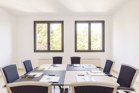 A meeting room at B&B Hotel Sassuolo with eight chairs surrounding a square table set with notebooks, pens, and folders under two windows
