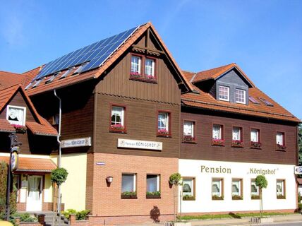 Building of Pension K&ouml;nigshof with brown wooden upper floors, red roof tiles and solar panels under a clear blue sky