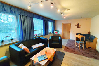 Living room area at Pension K&ouml;nigshof with black leather sofas, low table, decorated windows, and dining corner with wooden chairs and tablecloth