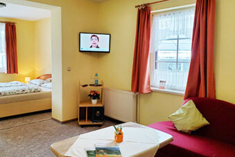 Room interior at Pension K&ouml;nigshof with a double bed, sofa, coffee table, curtains, and a wall-mounted television