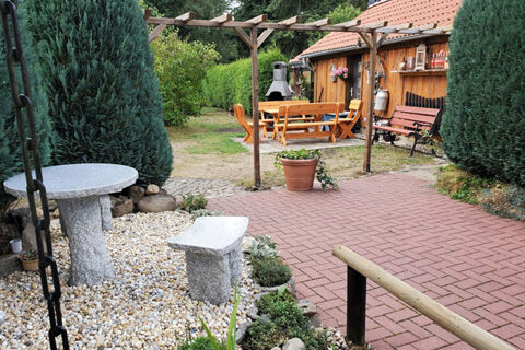 Outdoor seating area at Pension K&ouml;nigshof with stone table and bench, wooden dining set, and surrounding greenery and trees