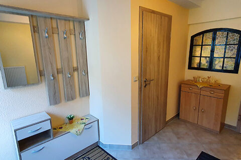 Entrance area of Pension K&ouml;nigshof with wooden coat hooks, gray storage bench, brown door, and a wooden cabinet under decorative window