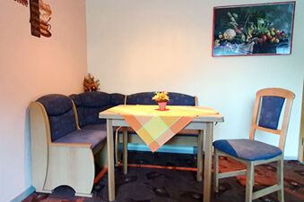 Corner seating with wooden frame and blue cushions around a table with a checkered tablecloth and flowers at Pension K&ouml;nigshof