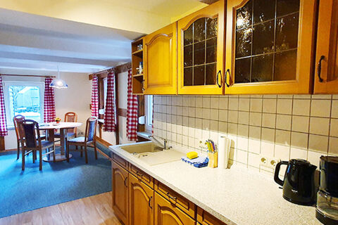 Kitchen and dining area at Pension K&ouml;nigshof with wooden cabinets, a countertop with appliances, a round table, and red checkered curtains