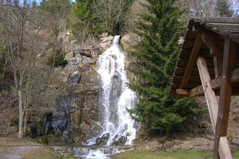 Waterfall flowing over rocky cliff surrounded by trees beside a wooden shelter near Pension K&ouml;nigshof
