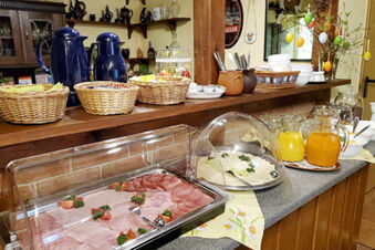Breakfast buffet on a countertop with cold cuts, cheese, juices, wicker baskets, and coffee pots at Pension K&ouml;nigshof
