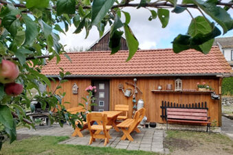 Wooden garden shed with red tile roof, outdoor table and chairs, bench, and apple tree in Pension K&ouml;nigshof garden
