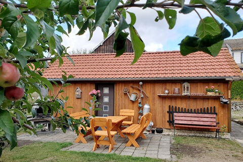 Wooden garden shed with red tile roof, outdoor table and chairs, bench, and apple tree in Pension K&ouml;nigshof garden