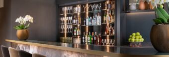 Modern bar interior at NH Collection Roma Giustiniano with hanging glasses, bottles of liquor, green apples, and flower vases