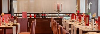 Dining area with purple chairs, dark wood tables, red glassware, candles, flowers, and menus at NH Collection Roma Giustiniano