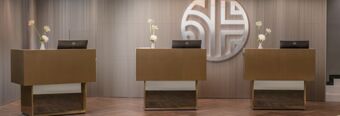 Three brown reception desks with Dell monitors and floral arrangements in front of a striped wall with a large circular logo at NH Collection Roma Giustiniano