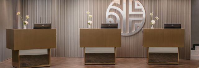 Three brown reception desks with Dell monitors and floral arrangements in front of a striped wall with a large circular logo at NH Collection Roma Giustiniano