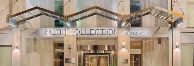 Entrance of NH Collection Roma Giustiniano hotel with illuminated modern metal canopy and revolving glass door at night