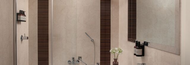 Bathroom interior at NH Collection Roma Giustiniano with beige walls, mounted shower products, bathtub, and a mirror above the sink