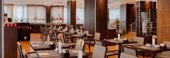 Dining area with wooden tables and chairs, each table adorned with vases and decor, at NH Collection Roma Giustiniano