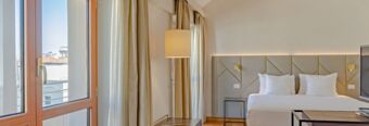 Hotel room at NH Collection Roma Giustiniano with a large bed, two bedside tables, a flat screen TV, and floor-to-ceiling windows