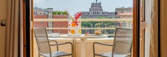 Two metal chairs and a round table with a drink and snacks on a balcony with a city view at NH Collection Roma Giustiniano