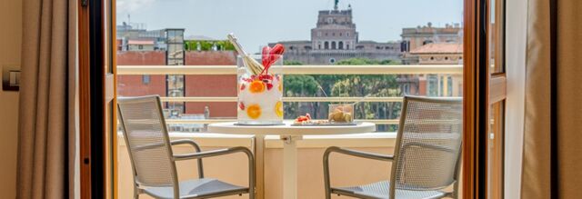 Two metal chairs and a round table with a drink and snacks on a balcony with a city view at NH Collection Roma Giustiniano