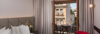 Hotel room interior at NH Collection Roma Giustiniano with a bed, pillows, bedside table, open door to balcony with table and chairs