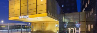 Modern glass and golden metal facade of NH Milano Fiera hotel at night with illuminated signage and entrance area visible