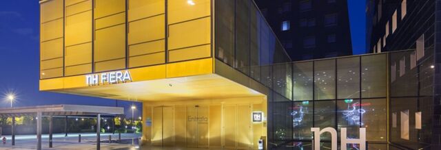 Modern glass and golden metal facade of NH Milano Fiera hotel at night with illuminated signage and entrance area visible