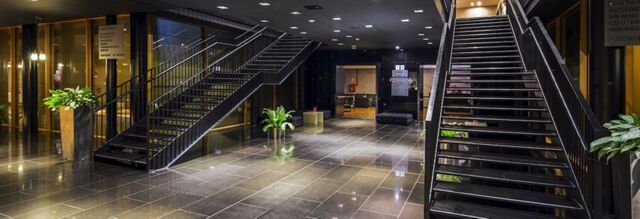 Interior view of the NH Milano Fiera lobby featuring two black metal staircases, polished tile floor, and potted plants