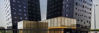 Modern dark glass twin towers rise behind a gold-trimmed glass entrance of the NH Milano Fiera hotel building