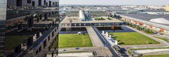 High angle view of modern black glass building and surrounding commercial structures near NH Milano Fiera hotel with water features and green lawns