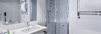 Modern bathroom at NH Milano Fiera with a white sink, large mirror, glass shower enclosure, and chrome towel rack