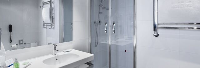 Modern bathroom at NH Milano Fiera with a white sink, large mirror, glass shower enclosure, and chrome towel rack