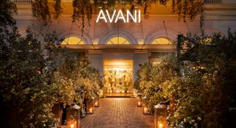Entrance to Avani Avani Palazzo Moscova Milan Hotel with illuminated sign, plants lining path, and glowing lanterns at dusk