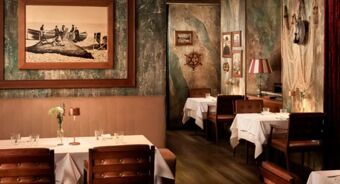 Dining tables with white tablecloths and wooden chairs in a rustic room decorated with old photos and a ship's wheel at Avani Avani Palazzo Moscova Milan Hotel