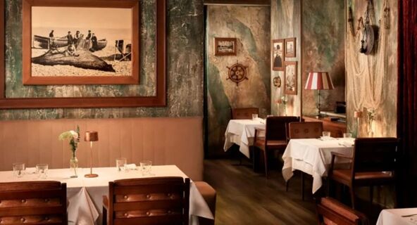 Dining tables with white tablecloths and wooden chairs in a rustic room decorated with old photos and a ship's wheel at Avani Avani Palazzo Moscova Milan Hotel