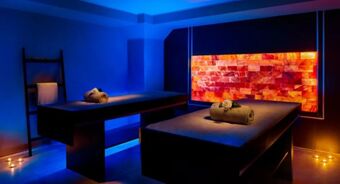 Two massage tables with rolled towels and a flower in a dimly lit spa room at Avani Avani Palazzo Moscova Milan Hotel